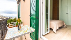 Un balcon avec une table dressée pour deux personnes, une porte verte et un lit à l’intérieur d’une pièce.