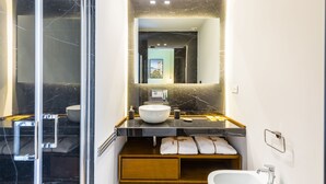 Une salle de bain moderne avec un grand miroir, un lavabo blanc, un bidet et une douche à parois de verre.