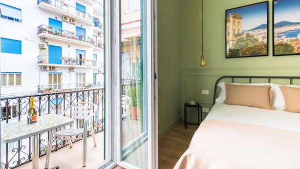 Une chambre avec un lit, une petite table et une chaise, ainsi qu’un balcon avec une table et des chaises.
