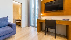 A modern hotel room with a wooden desk, a flat-screen TV, a blue sofa, and a window with curtains. - B&B Civico 33 - Parthenope Qdpl (Napoli)