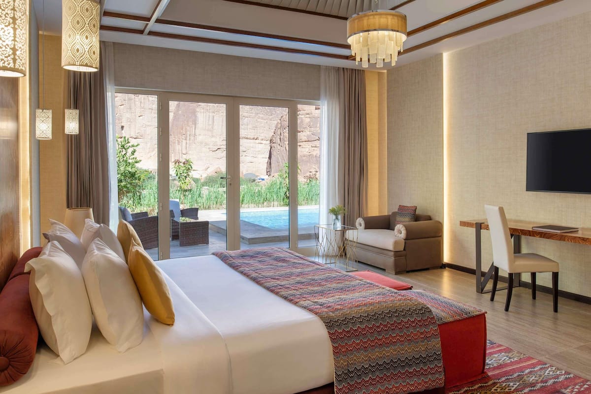 A hotel room with a bed, a desk, a TV, and a view of a pool and outdoor area.