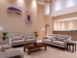 A spacious lobby with two sofas, a coffee table, and a small side table. There are two potted plants and artwork on the walls.