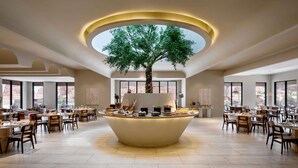 Un amplio comedor con una isla central que tiene un árbol, rodeado de varias mesas y sillas.
