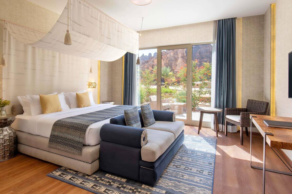 Una habitación de hotel moderna con una cama grande, un sofá, una mesa de comedor y un balcón con vistas al exterior.