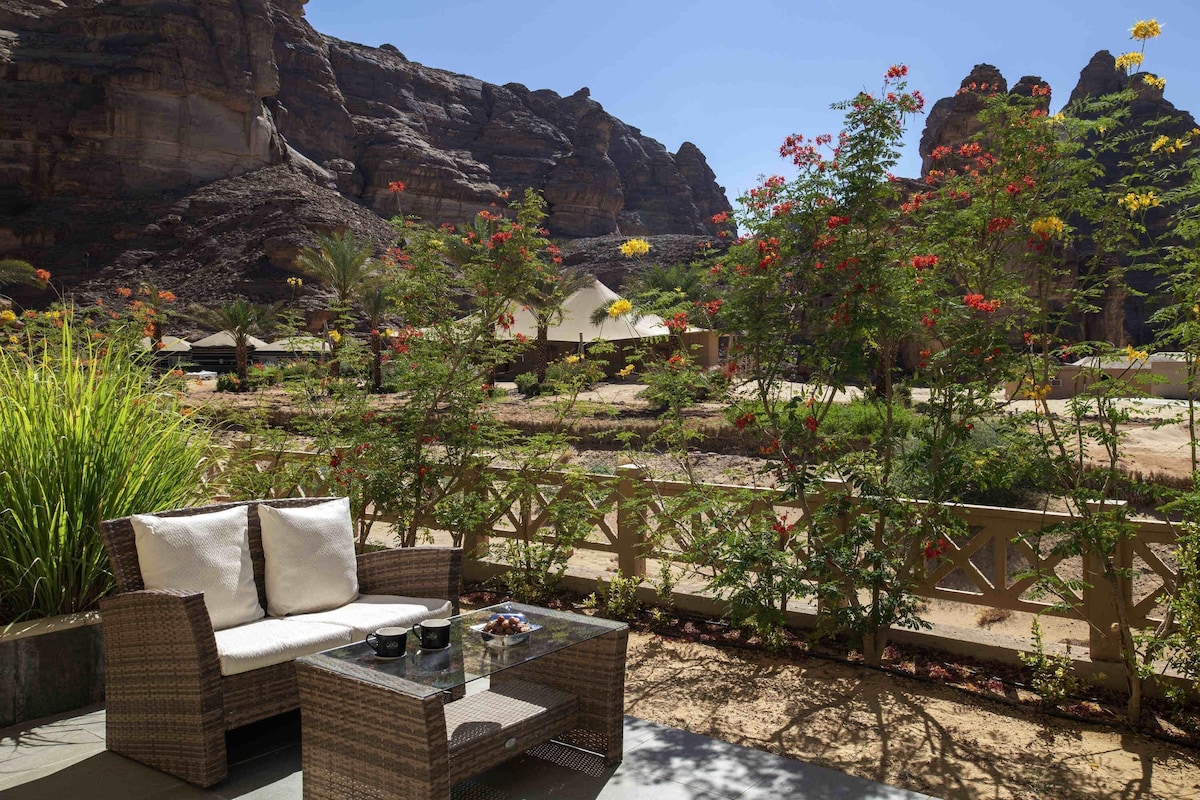 A patio with wicker furniture, a glass-top table, and a view of rock formations.