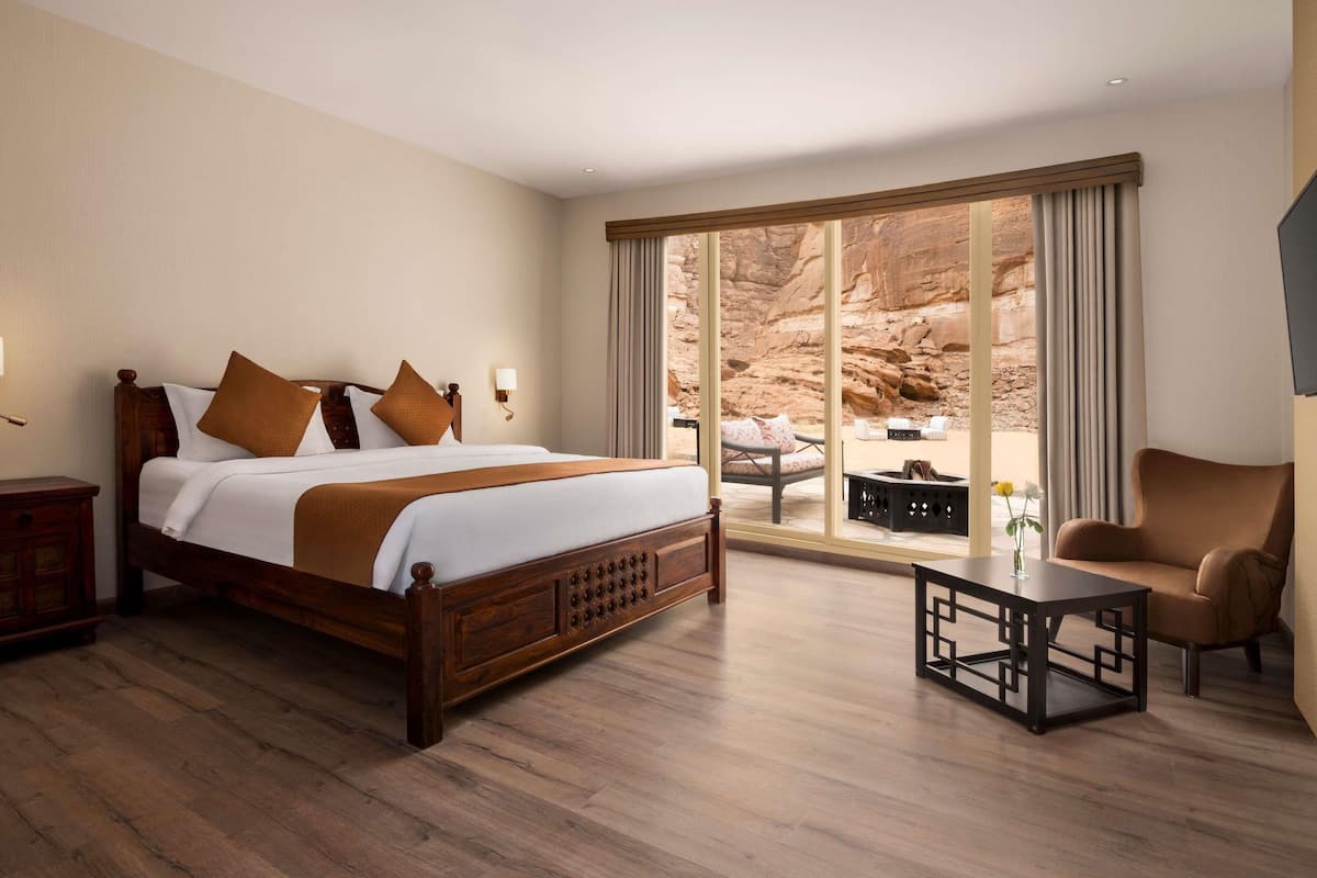 A hotel room with a large bed, a seating area with a chair and table, and a view of a canyon through a sliding door.
