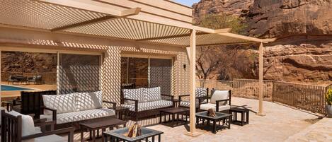 Eine Terrasse im Freien mit Sitzgelegenheiten, einer Pergola und Blick auf felsiges Gelände.