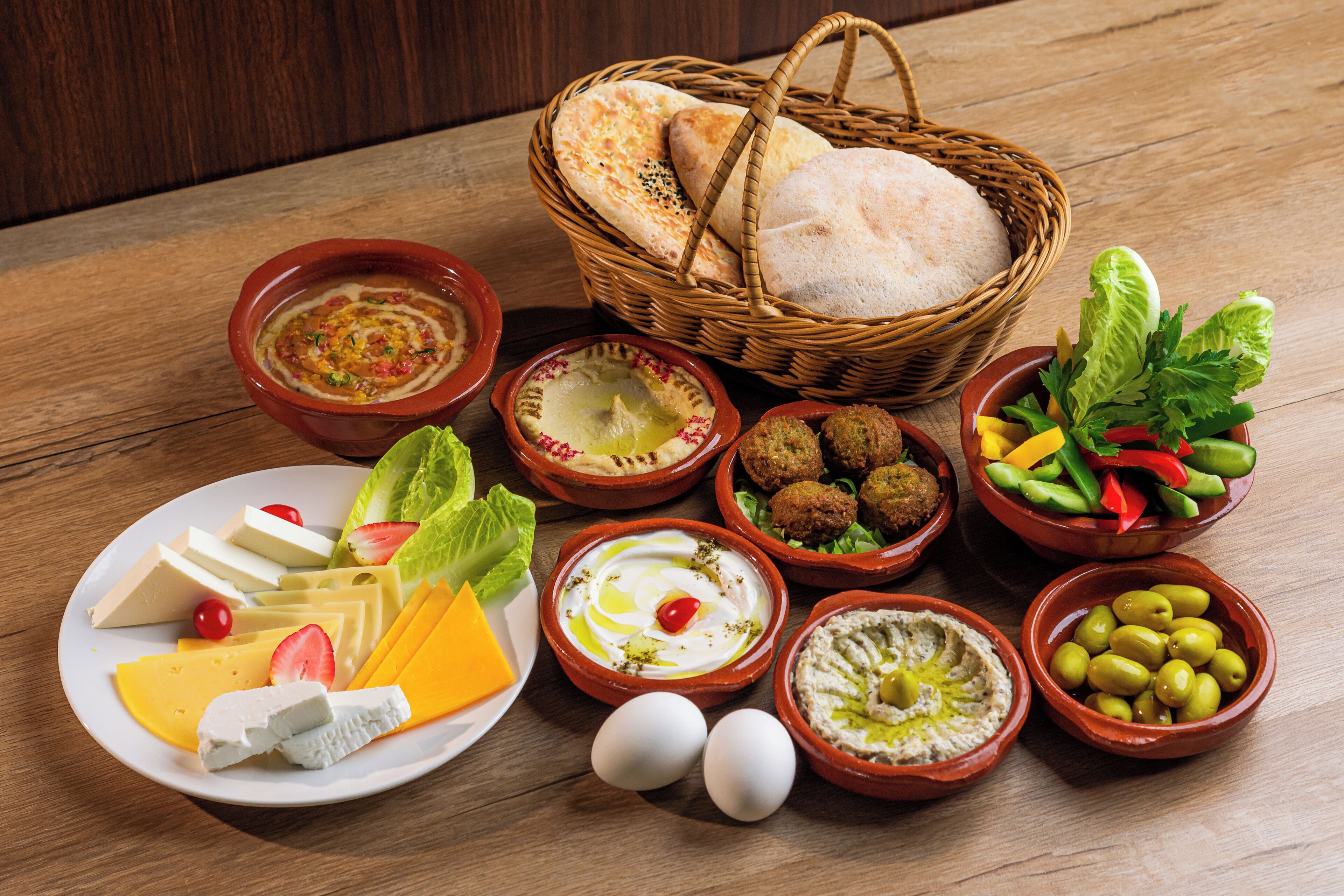 A variety of food items including bread, cheese, olives, and vegetables on a wooden table.