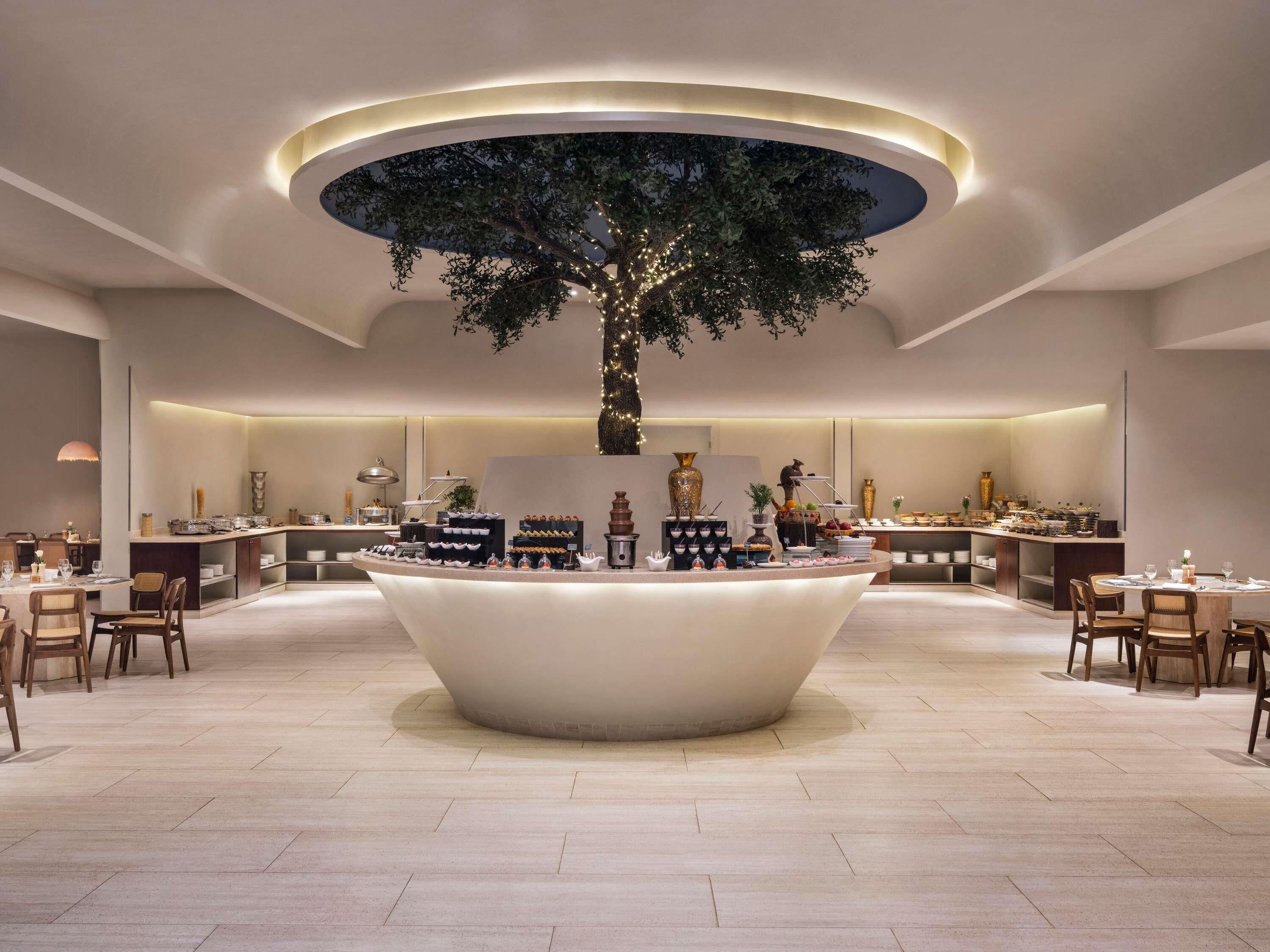 A modern hotel lobby with a central island featuring a tree and a buffet.