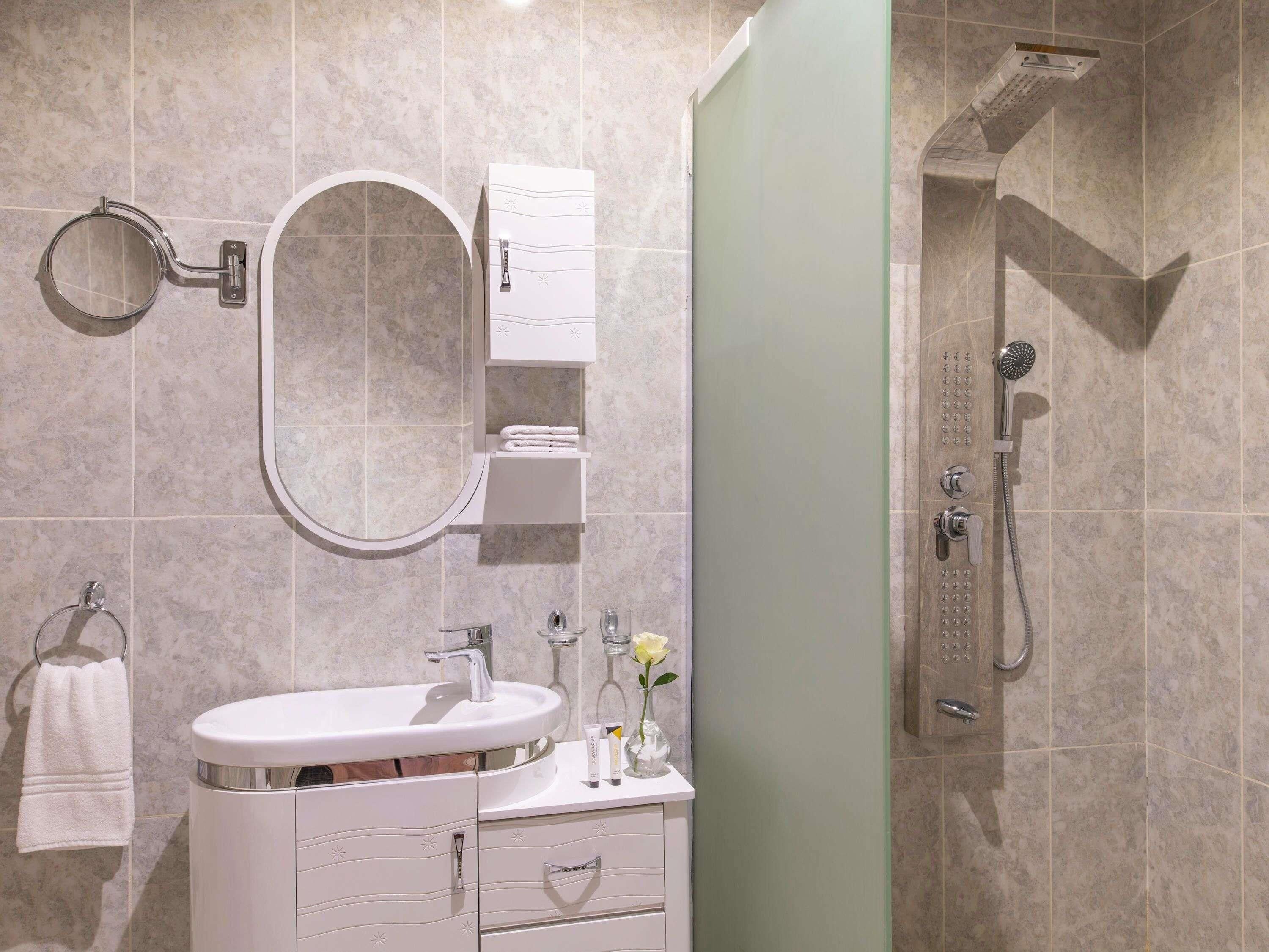 A bathroom with a sink, mirror, towel rack, and shower.
