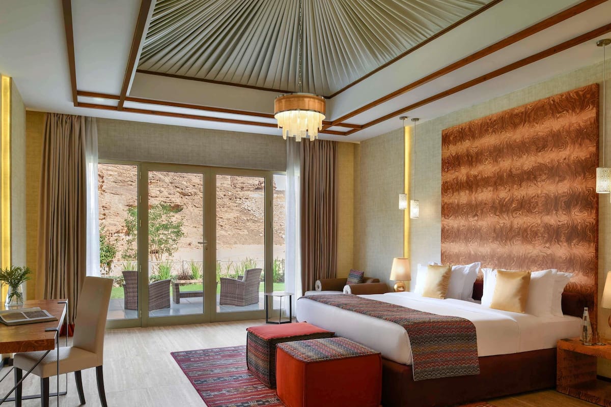 A hotel room with a large bed, a desk with a chair, a dining table, and a view of the outdoors.