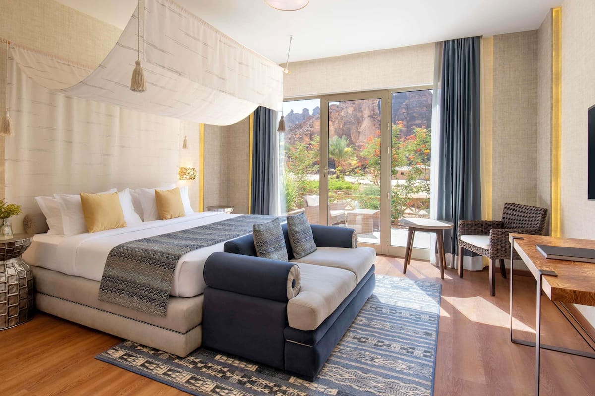 Una habitación de hotel moderna con una cama grande, un sofá, una mesa de comedor y un balcón con vistas al exterior.