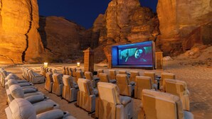 Cine al aire libre con hileras de sillones acolchados y una pantalla grande en un entorno desértico.