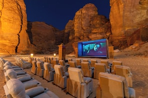 An outdoor cinema with rows of cushioned chairs and a large screen in a desert setting. - Shaden Resort Al Ula, Managed by Accor (Al-'Ula)