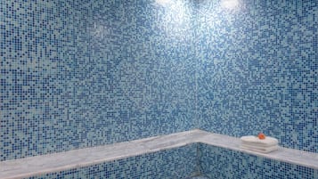 A bathroom with blue mosaic tiles, a white bathtub, and a towel rack with a towel and a rose.