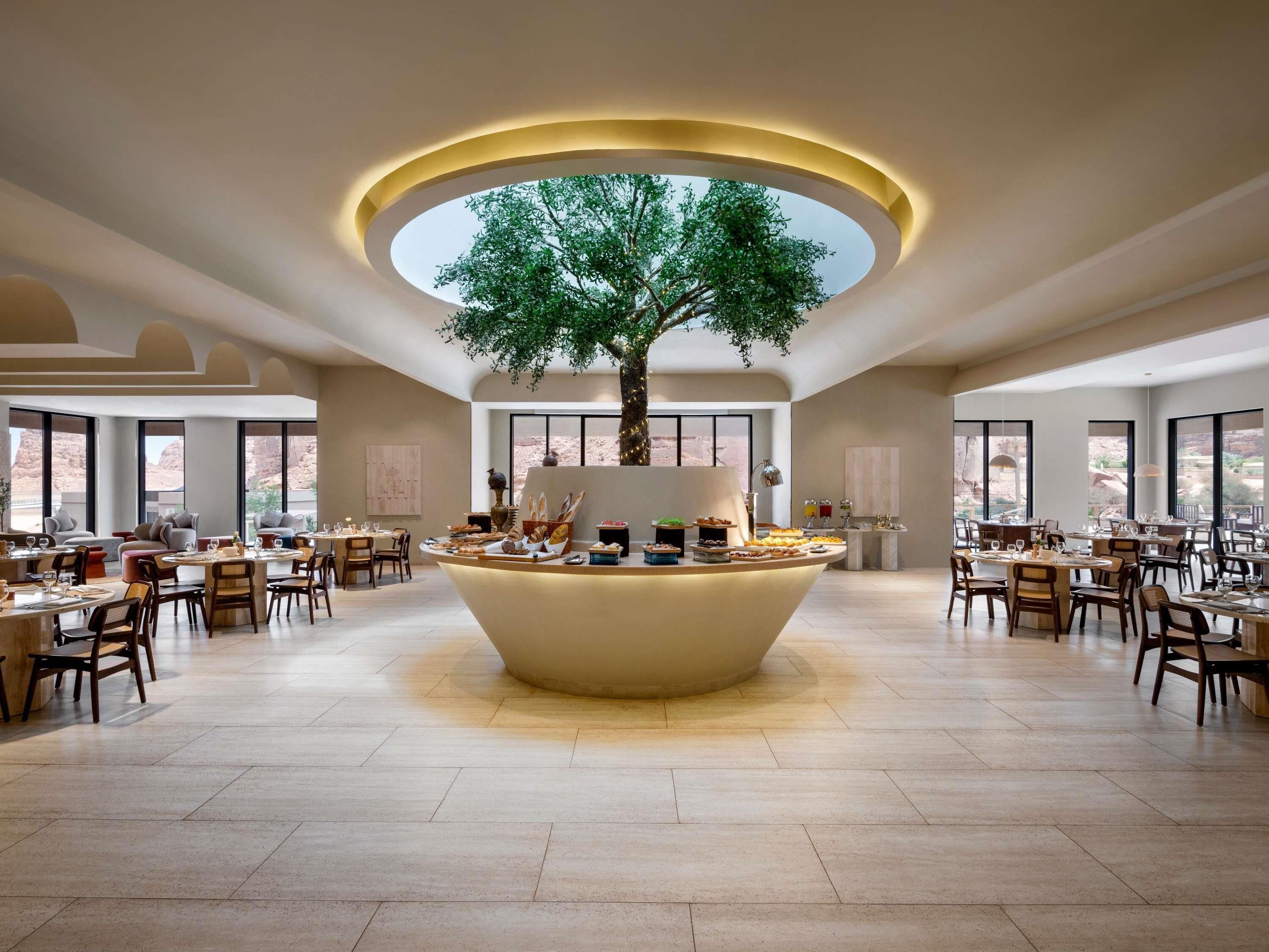Un amplio comedor con una isla central que tiene un árbol, rodeado de varias mesas y sillas.
