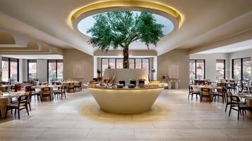 Un amplio comedor con una isla central que tiene un árbol, rodeado de varias mesas y sillas.