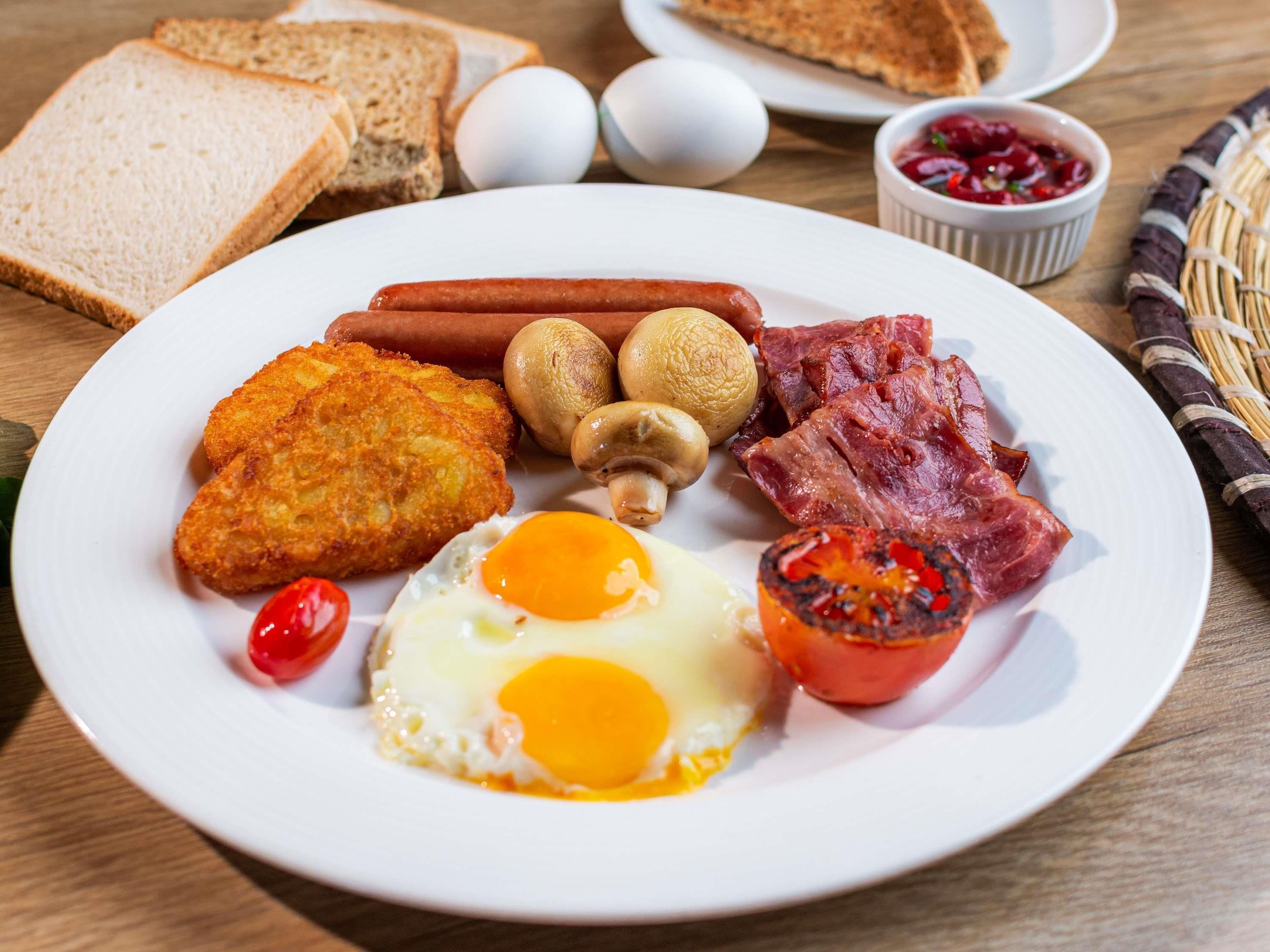 Ein Frühstücksteller mit Eiern, Würstchen, Speck, Pilzen und Toast.