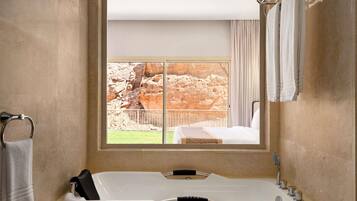 A bathroom with a large bathtub, a window with a view of rocky terrain, and a towel rack.