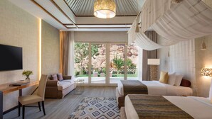 Habitación de hotel con una cama grande, un escritorio con una silla, un televisor y vista a un jardín por una puerta corredera.