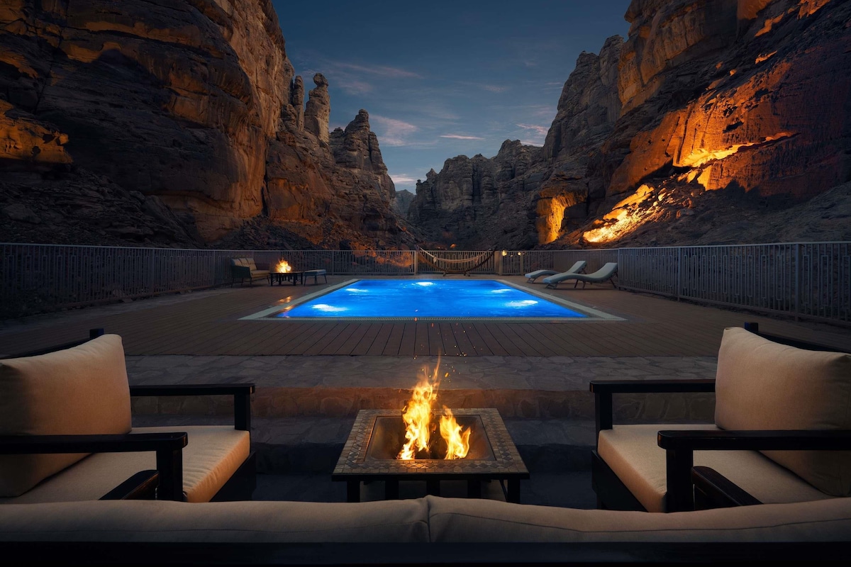 A pool area with a fire pit and lounge chairs, surrounded by rocky cliffs.