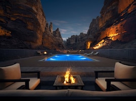 Zona de piscina con una chimenea y sillones de descanso, rodeada de acantilados rocosos.