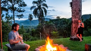 Two people sitting by a campfire with a mountainous landscape in the background. - Fazenda Ressaca: Natural Luxury (Ubatuba)