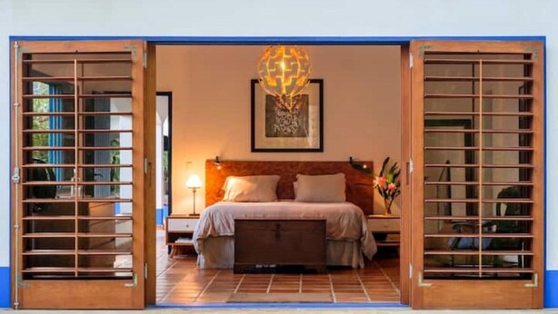 A bedroom with a bed, nightstands, a lamp, and a wall-mounted artwork. - Fazenda Ressaca: Natural Luxury (Ubatuba)