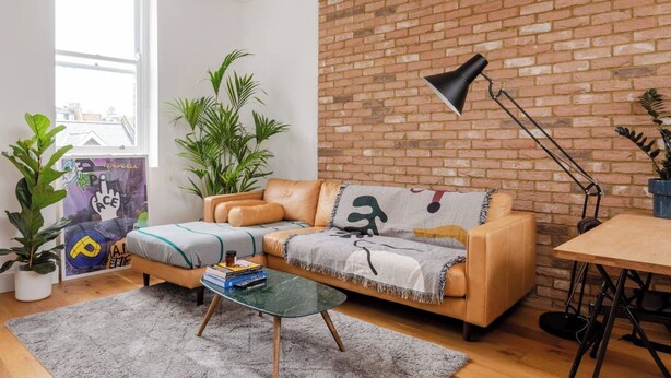 A modern living room with a brick wall, leather sofa, glass coffee table, and potted plants. - Hackney Haven Modern 1 BDR Wifi (London)