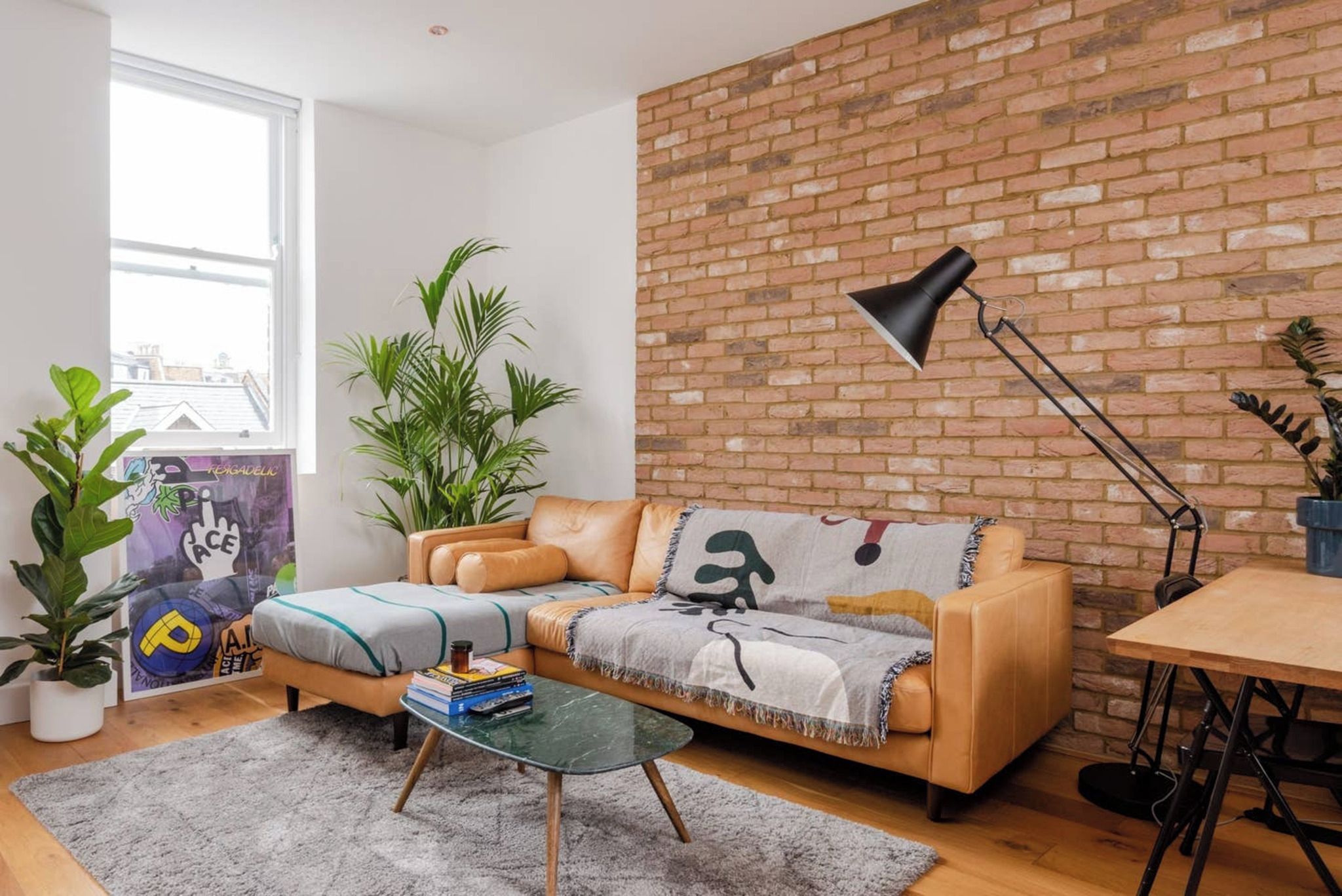 A modern living room with a leather sofa, a glass coffee table, and a brick wall.