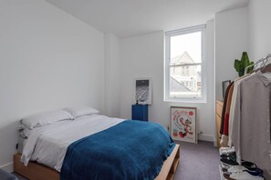 Une chambre avec un lit, une fenêtre, une affiche et un portant à vêtements.