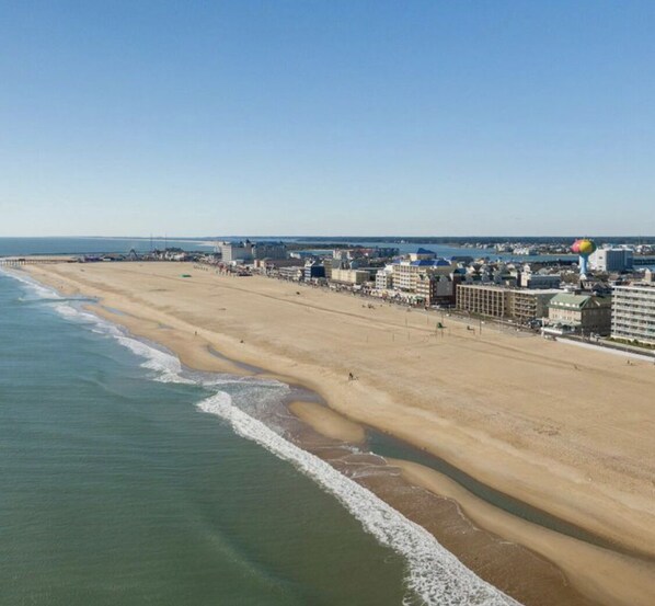 Una playa con una extensa franja de arena, algunos edificios y una torre de agua a lo lejos.