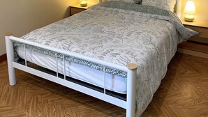 A neatly made bed with a floral pattern, two bedside lamps, a framed picture on the wall, and a herringbone wooden floor. - 17th century property between the pink granite coast & Lannion, Studio 27m2  (Saint Quay Perros)