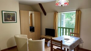A room with a wooden wardrobe, a television on a small table, two white chairs, a table with a tablecloth, and a large window with curtains. - 17th century property between the pink granite coast & Lannion, Studio 27m2  (Saint Quay Perros)