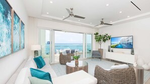 A modern living room with a sofa, chairs, a TV, and a balcony with a view of the sea. - Rum Point Club #306 (North Side)