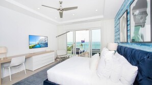 A hotel room with a bed, a desk, a chair, a TV, and a balcony with a view of the sea. - Rum Point Club #306 (North Side)