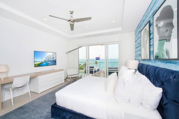 A hotel room with a bed, a desk, a chair, a TV, and a balcony with a view of the sea. - Rum Point Club #306 (North Side)