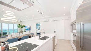 A modern kitchen with a central island, stainless steel appliances, and a view of the sea. - Rum Point Club #306 (North Side)