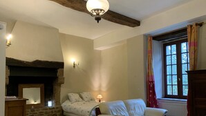 Une pièce chaleureuse avec une cheminée en pierre, un canapé, un lit et une fenêtre avec des rideaux.