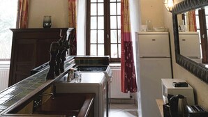 Une cuisine de taille réduite avec un plafond orné de poutres en bois, une fenêtre avec des rideaux, un réfrigérateur, un four à micro-ondes et un évier.