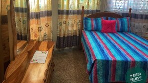 A bedroom with a wooden dresser, a bed with striped bedding, and curtains with floral patterns. - Areca Palms (Port Antonio)