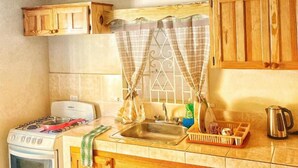 A kitchen with wooden cabinets, a stove, a sink, and a window with curtains. - Areca Palms (Port Antonio)