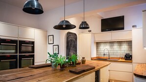 A modern kitchen with a wooden island, built-in ovens, a large black TV, and pendant lighting. - Lonsdale Villa Retreat (Penrith)