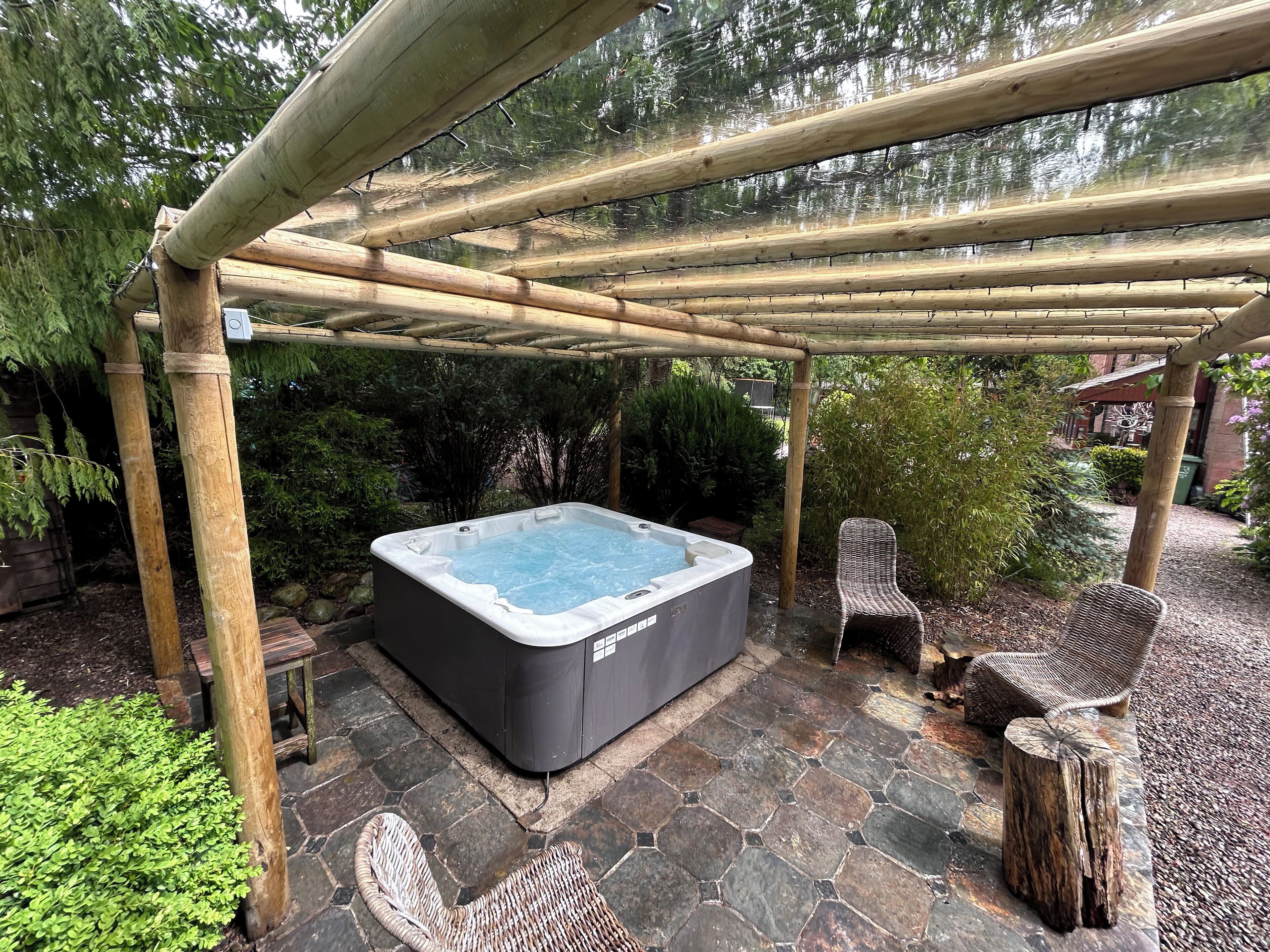 Ein Whirlpool unter einem Bambus-Pergola in einem Garten mit Steinboden und Korbstühlen.
