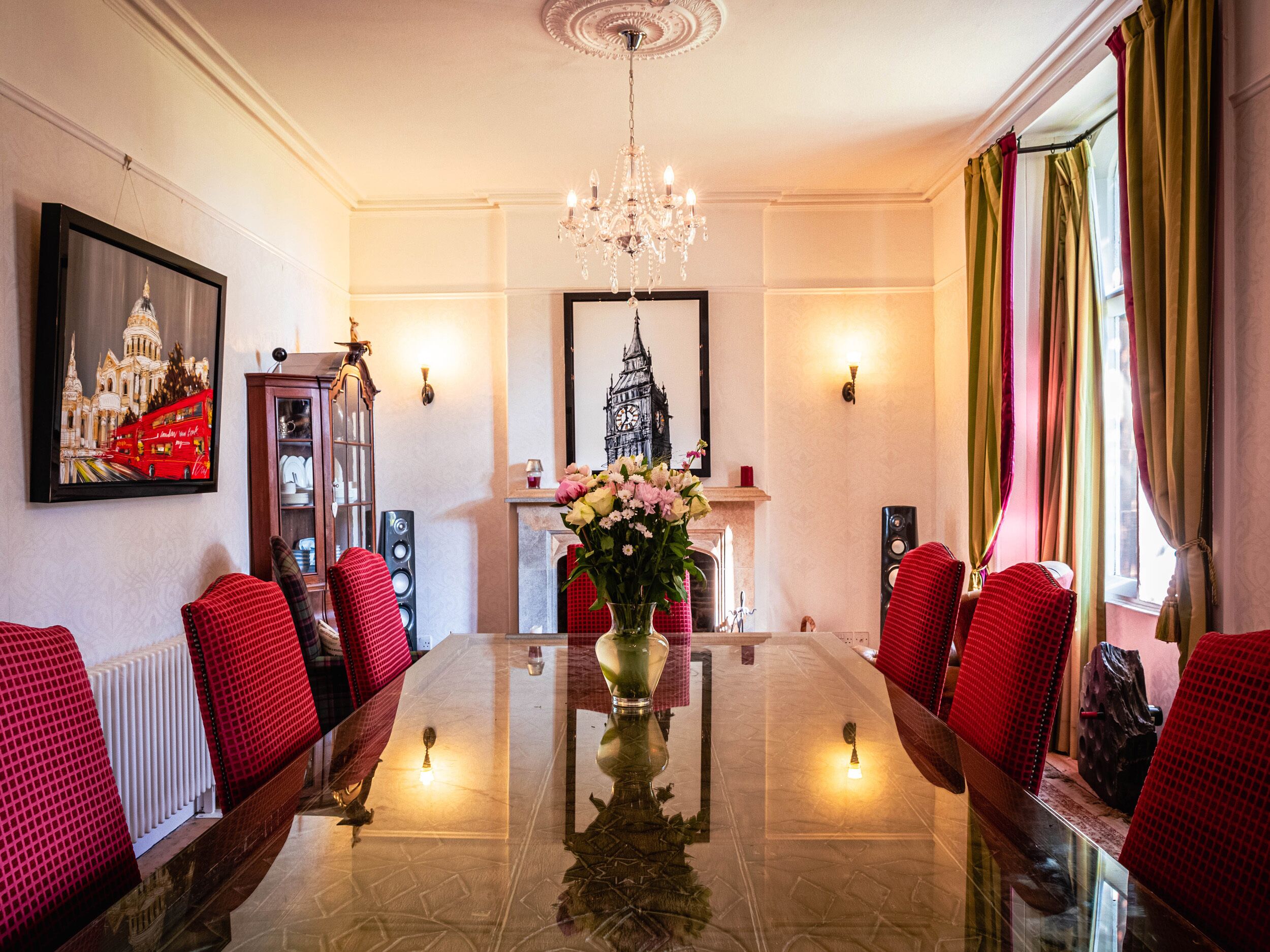 Ein formeller Speisesaal mit einem langen Tisch, roten, gepolsterten Stühlen, einer Chandelierleuchtre und Kunstwerken an den Wänden.