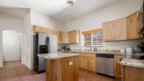 Een moderne keuken met houten kastjes, een centraal eiland, roestvrijstalen apparatuur en een betegelde vloer.
