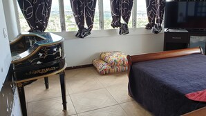 Ein Hotelzimmer mit Bett, Schreibtisch mit Klavier, Fernseher und Blick auf die Stadt durch das Fenster.
