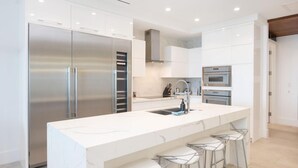 A modern kitchen with a large island, stainless steel appliances, and bar stools. - Rum Point Club #304 (North Side)
