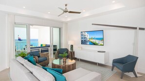 A modern living room with a sofa, chairs, a coffee table, a TV, and a balcony with a view of the sea. - Rum Point Club #304 (North Side)