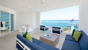 A modern living room with a balcony overlooking the sea, featuring a sofa set, a dining table, and ceiling fans. - Rum Point Club #304 (North Side)